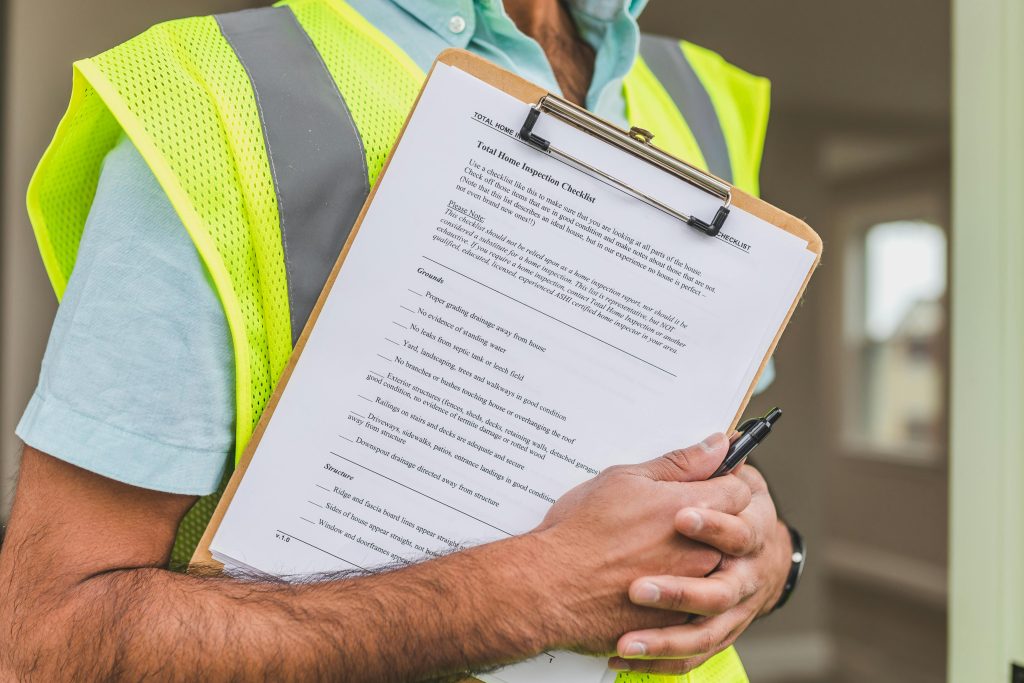 An inspector wearing a green vest with a home inspection checklist on his hands.